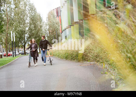 Lächelndes Paar zu Fuß mit dem Fahrrad auf der Spur Stockfoto