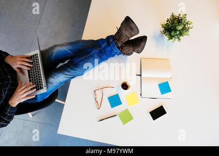 Geschäftsmann mit Laptop mit den Füßen auf dem Schreibtisch im Büro Stockfoto