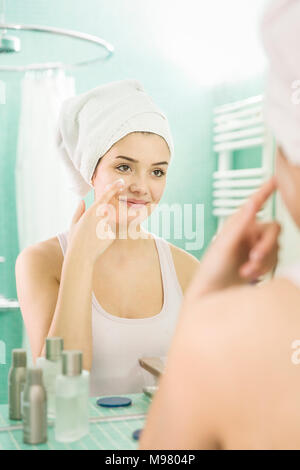 Junge Frau Anwendung gesichtsfeuchtigkeitscreme am Spiegel im Bad Stockfoto