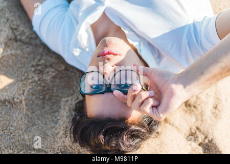Porträt eines jungen Mannes mit Brille im Sand am Strand liegen Stockfoto