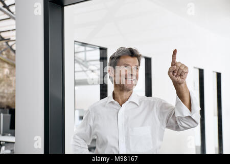 Lächelnd reife Geschäftsmann berühren Glasscheibe in modernen Büro Stockfoto