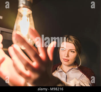 Junge Frau erreichen für leuchtende Glühbirne Stockfoto