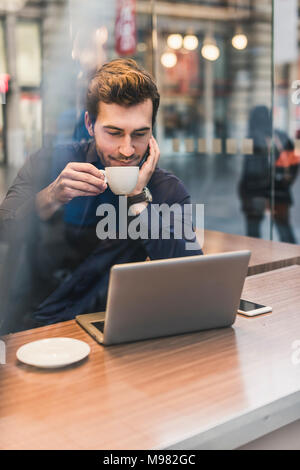 Junge Unternehmer in einem Café am Bahnhof mit Tasse Kaffee und Laptop Stockfoto