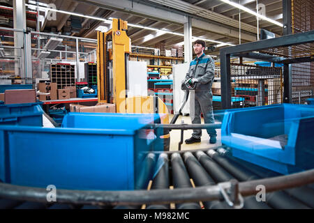 Mann bei der Arbeit in der Fabrik mit Boxen auf Transportband Stockfoto