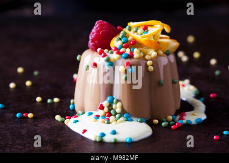 Schokoladenpudding und Vanillesoße garniert mit Himbeere, Orange und Zucker Perlen Stockfoto