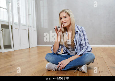 Portrait von lächelnden blonde Frau auf dem Boden sitzend mit Handy Stockfoto