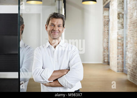 Portrait von lächelnden Geschäftsmann lehnte sich gegen Glasscheibe in modernen Büro Stockfoto