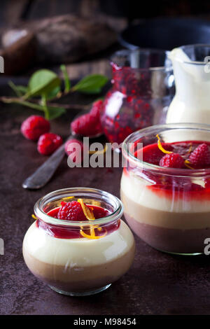 Gläser Pudding mit Vanillesoße und Himbeersauce garniert mit Himbeeren und Orangenschale Stockfoto