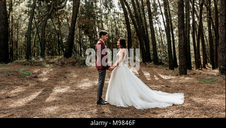 Braut und Bräutigam stehen im Wald halten sich an den Händen Stockfoto
