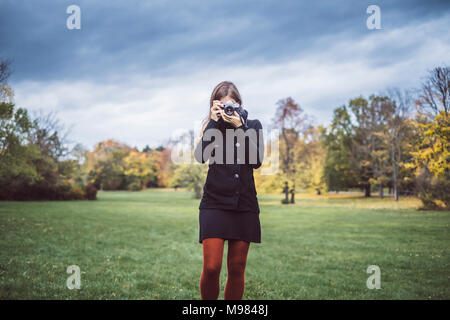 Junge Frau Aufnehmen von Bildern mit der Kamera auf einer Wiese im herbstlichen Park Stockfoto