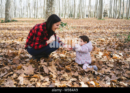 Mutter und Baby Mädchen spielen mit Blätter im Herbst Blätter in Park Stockfoto