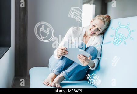Frau sitzt im Büro, mit digitalen Tablet auf remote-control seine Smart Home Stockfoto