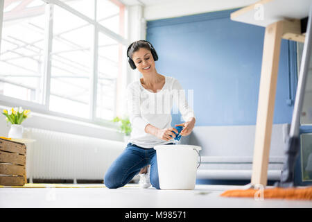 Lächelnde Frau zu Hause mit Kopfhörern wischen den Boden Stockfoto