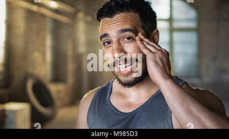 Muskulöse Mann Scheibenwischer Schweiß von seiner Stirn nach intensiven Cross Fitness Bodybuilding Training. Er lächelt charmant. Er trägt Ärmelloses Shirt Stockfoto