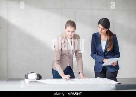 Zwei junge Frauen mit Tablet- und VR-Brille arbeiten an Blueprint im Büro Stockfoto