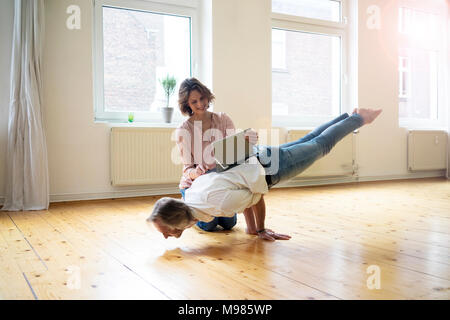 Reife Frau mit Tablett auf der Rückseite der Mann macht einen Handstand Stockfoto