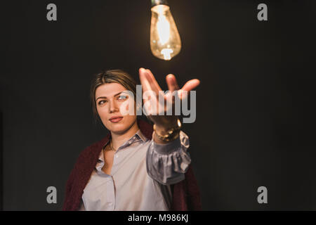 Junge Frau erreichen für leuchtende Glühbirne Stockfoto