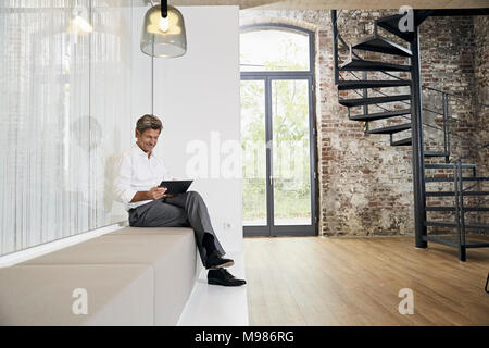 Geschäftsmann sitzt auf der Bank im modernen Office mit Tablet Stockfoto