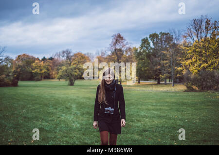 Junge Frau mit Kamera zu Fuß auf einer Wiese im herbstlichen Park Stockfoto