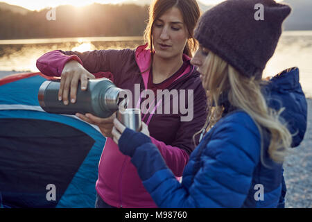 Zwei Frauen mit heißen Getränk camping am Seeufer Stockfoto