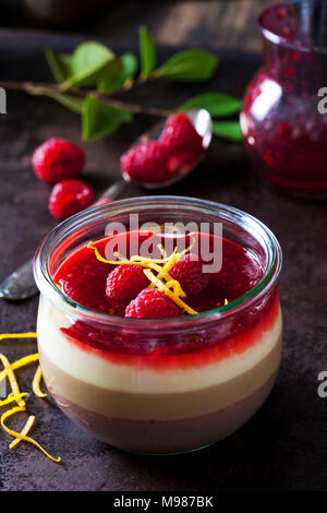 Glas Pudding mit Vanillesoße und Himbeersauce garniert mit Himbeeren und Orangenschale Stockfoto