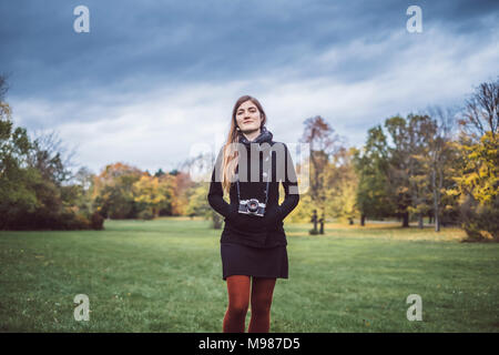 Porträt der jungen Frau mit Kamera zu Fuß auf einer Wiese im herbstlichen Park Stockfoto