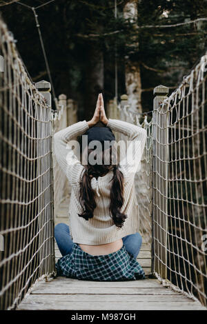 Junge Frau in Yoga pose sitzen auf einer Hängebrücke Stockfoto