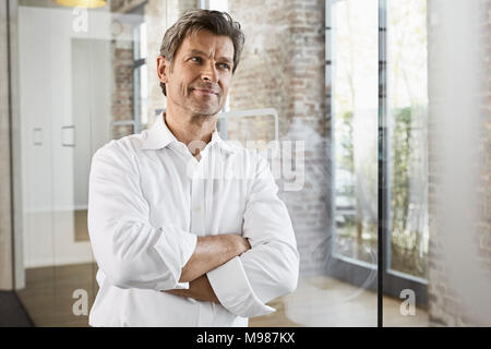 Portrait von Reifen Geschäftsmann lehnte sich gegen Glasscheibe in modernen Büro Stockfoto