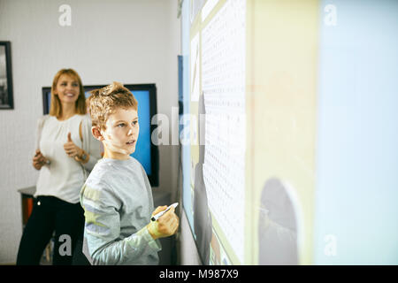 Schüler in der Klasse auf der interaktiven Whiteboard mit Lehrer im Hintergrund Stockfoto