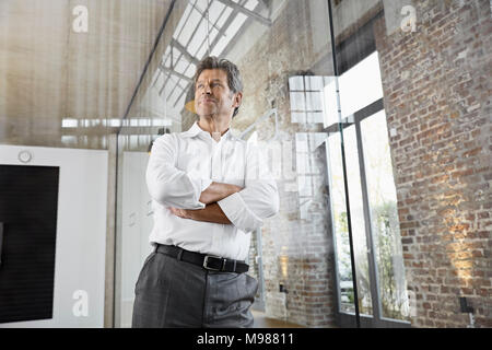 Portrait von Reifen Geschäftsmann lehnte sich gegen Glasscheibe in modernen Büro Stockfoto