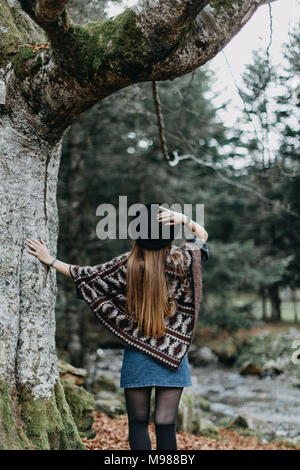 Rückansicht der jungen Frau mit Hut und Poncho im herbstlichen Wald Stockfoto