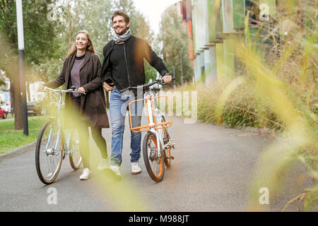 Lächelndes Paar zu Fuß mit dem Fahrrad auf der Spur Stockfoto