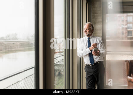 Lächelnd reife Geschäftsmann stand am Fenster Stockfoto