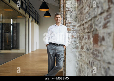 Portrait von zuversichtlich Geschäftsmann lehnte sich gegen die Mauer in modernen Büro Stockfoto