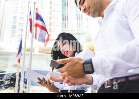 Thailand, Bangkok, Geschäftsmann und Geschäftsfrau in der Stadt mit Dokumenten, Handy und smartwatch Stockfoto