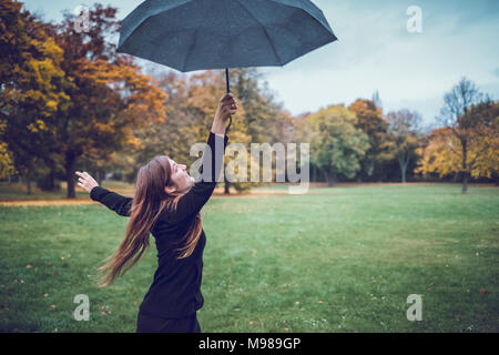 Glückliche junge Frau tanzen mit Regenschirm im herbstlichen Park Stockfoto