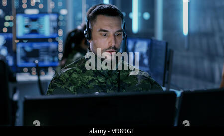 Nahaufnahme der militärischen Technischer Support Professional gibt Anweisungen über das Headset. Er ist in einem Zimmer mit anderen Offizieren Stockfoto