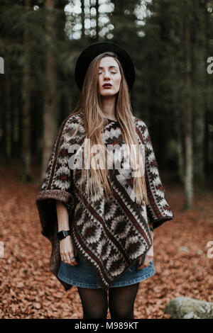 Porträt der jungen Frau mit Hut und Poncho stehen im herbstlichen Wald Stockfoto