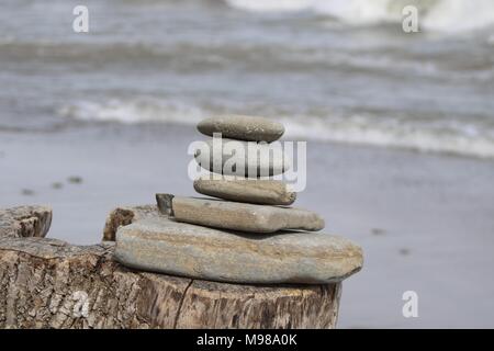 Steine auf einem Baumstumpf mit Blick auf die kommenden Wellen ausgerichtet Stockfoto