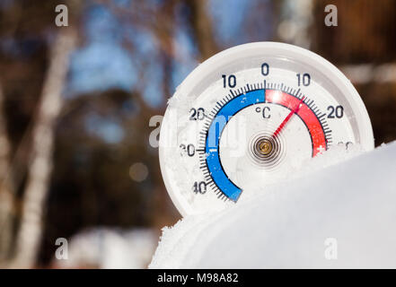 Thermometer with celsius scale in melting snow showing plus 12 degree temperature warm spring weather or global warming concept Stockfoto