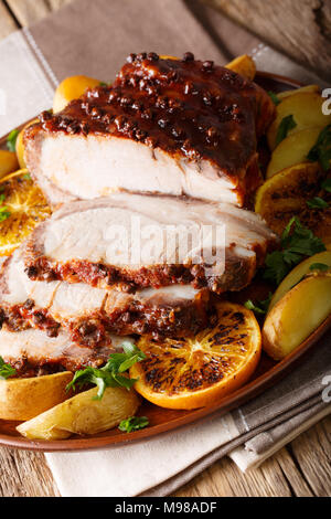 Weihnachten gebackenes Schweinefleisch mit Kartoffeln, Orangen und Äpfel Close-up auf einem Teller. Vertikale Stockfoto