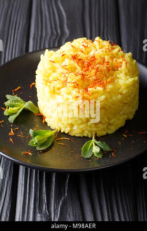 Traditionelle risotto alla milanese mit Safran ist mit Minze closeup auf einem Teller auf den Tisch dekoriert. Vertikale Stockfoto