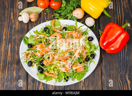 Hohe Betrachtungswinkel und der Salat mit Mix aus Salatblättern, Garnelen, Oliven und Dijon Senf, Dressing in weiße Platte auf hölzernen Schreibtisch Stockfoto