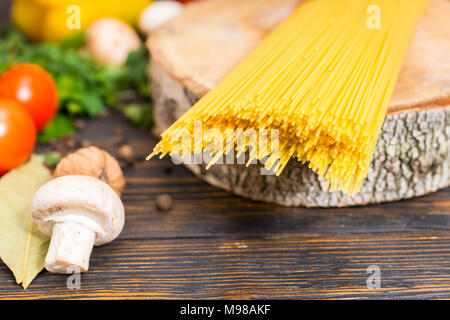 Gelb lange Spaghetti auf Holz Stativ in Form von Hanf in der Nähe von Gemüse auf hölzernen Schreibtisch Stockfoto