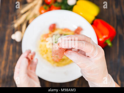 Hohe Betrachtungswinkel der Hände in Handschuhen holding Jamon oben spaghetti Pasta mit Garnelen, geriebenem Käse, Tomatensoße und Basilikum in weißen Platten umgeben von Stockfoto