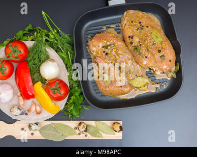 Hohe Betrachtungswinkel von mariniertes Hähnchenfleisch auf einem Pan in der Nähe von Gemüse, Wachteleier auf einem Holzbrett auf einem grauen Schreibtisch Stockfoto