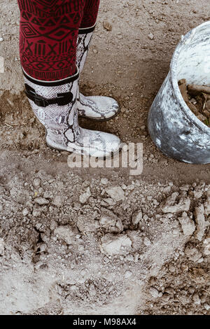 Menschliche Beine in Gummistiefel und alten Eimer in Farbe mit Steine und Unkraut in den fallenden, nach der Reinigung. Konzept arbeiten, kopieren. Film Effekt. Stockfoto