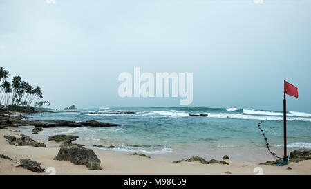 Blick auf Meer und Sandstrand in Sri Lanka bei Sturm. Red Flag Kennzeichnung gefährlicher Ort zum Schwimmen im Wasser Stockfoto