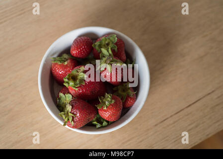 Overhead Shot von Erdbeeren in Weiß Schüssel auf hellem Holz Tisch oben Stockfoto