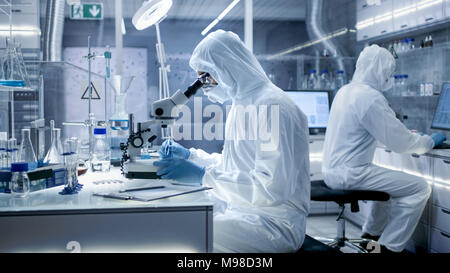 In einem sicheren Hohe Labor Wissenschaftler in einem Overall, die Durchführung einer Forschung. Biologe passt die Proben in eine Petrischale mit einer Zange und untersucht Stockfoto